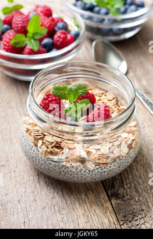 Dieta sana prima colazione. Budino di Chia con muesli, Lamponi Mirtilli in una ciotola di vetro, frutti di bosco freschi su sfondo di legno Foto Stock