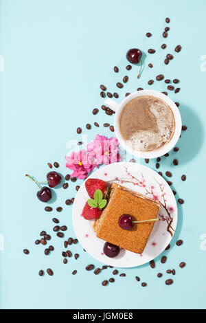 Gustoso pezzo di torta sulla piastra bianca e la tazza di caffè,decorato con fiori,i chicchi di caffè,fragole e ciliegia sulla luce Sfondo menta con Foto Stock