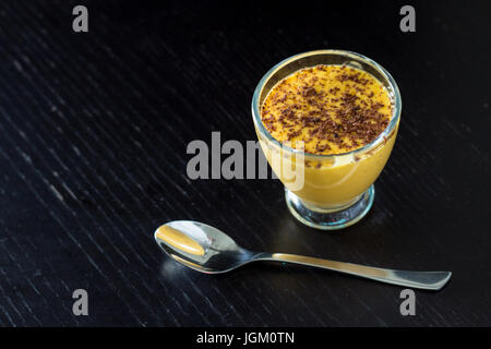 Mango lassi è un famoso Indian rinfrescante bibita salutare fatta di mango, lo yogurt e il cardamomo e decorate con il cioccolato. Su un nero lo sfondo di legno Foto Stock