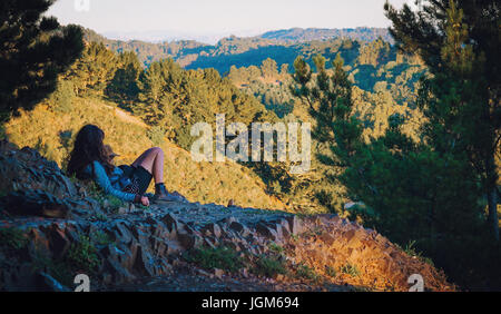 Ragazza che giace sulla cima di una collina che guarda sopra la foresta sottostante Foto Stock