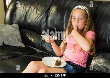 Ragazza giovane e carina gode di mangiare il dessert sul lettino Foto Stock