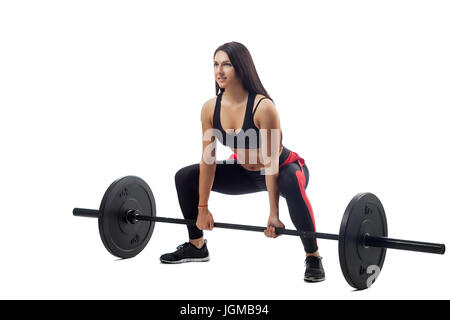 Atletica Giovane donna bruna facendo uno squat con un barbell su un bianco sfondo isolato, vista laterale, gambe stand ampia, in posizione seduta, close-up Foto Stock