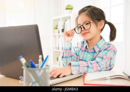 Seriamente e focalizzato kid guardando il computer portatile in seduta Scrittorio di studio toccato a mano bicchieri e sorridente. Asian i bambini si sentono l'e-learning divertente. Foto Stock