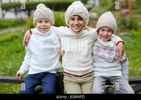 Tre ragazzi felici giocando all'aperto in campagna, che pongono alla telecamera seduto sulla staccionata in legno e sorridente godendo di giorno di autunno caldo Foto Stock