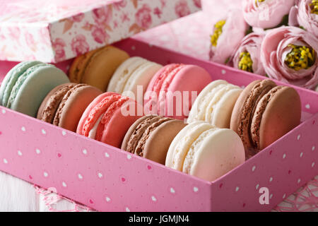 Amaretti al francese in un riquadro rosa e fiori close-up su una tavola orizzontale. Foto Stock