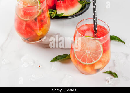 Estate cocktail e bevande. La limonata, in casa di sangria con fresco cocomero, lime, menta e ananas. In due bicchieri, su un marmo bianco tavola. Cop Foto Stock