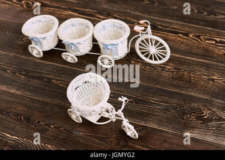Il triciclo cesti di fiori su legno. White giocattoli di plastica. A buon mercato gli articoli domestici della decorazione. Foto Stock
