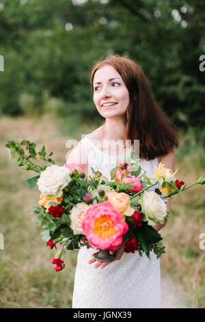 Bellezza, Wedding, molla, natura, il concetto di decorazione - shapely donna sorridente con il marrone scuro capelli in white party dress con colorati mazzo composto o Foto Stock