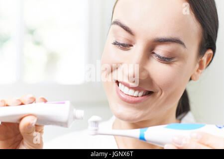 La donna la spremitura di dentifricio sullo spazzolino da denti elettrico nella stanza da bagno Foto Stock