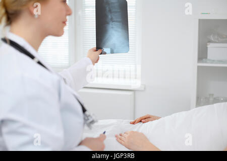 Medico donna esamina un X-ray immagine della colonna vertebrale accanto al paziente sdraiato sul letto in ospedale. Foto Stock