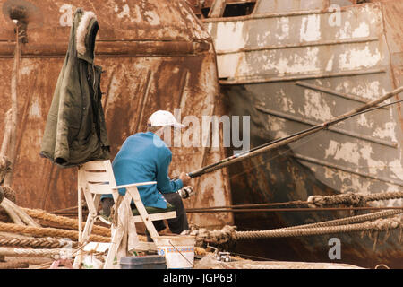 Uomo anziano la pesca nei pressi di arrugginire le navi per la pesca a strascico nel porto spagnolo Foto Stock