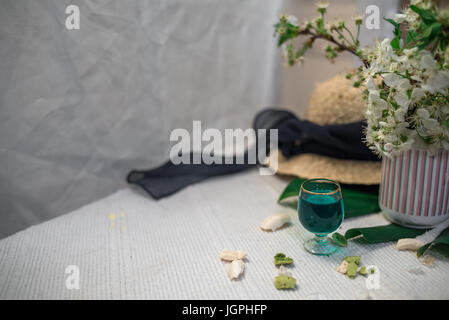 Un bicchiere di assenzio su uno sfondo bianco con un foglio di mostri e un cappello di paglia Foto Stock