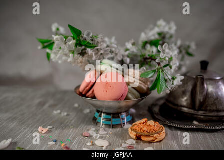 Amaretti multicolore su una tabella con vaso orientale e il ramo di ciliegio in fiore Foto Stock