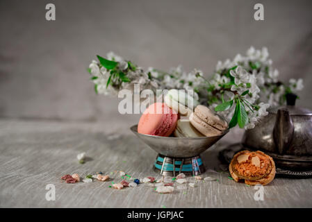 Amaretti multicolore su una tabella con vaso orientale e il ramo di ciliegio in fiore Foto Stock