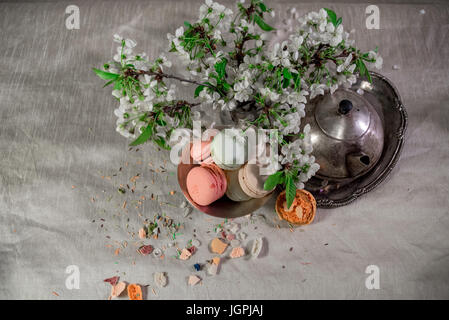 Amaretti multicolore su una tabella con vaso orientale e il ramo di ciliegio in fiore Foto Stock