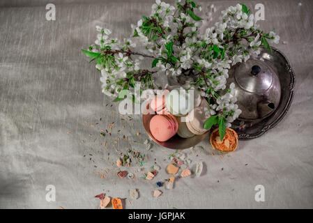 Amaretti multicolore su una tabella con vaso orientale e il ramo di ciliegio in fiore Foto Stock