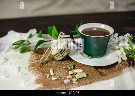 Una tazza di caffè su un vassoio bianco con il ramo di ciliegio sbocciato e foglia di monstera Foto Stock