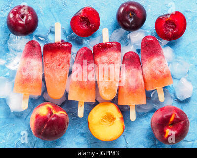 Vista dall'alto di susina e pesca ghiaccioli su sfondo blu. Popsicles frutta gelato con prugne fresche e pesca. Foto Stock