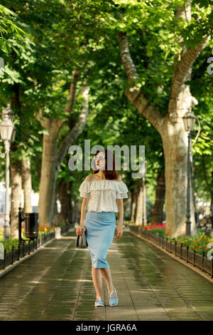 Giovane donna sta camminando in un parco in una camicia bianca e una matita blu gonna. Messa a fuoco selettiva. Foto Stock