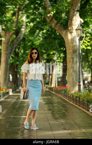 Giovane donna sta camminando in un parco in una camicia bianca e una matita blu gonna. Messa a fuoco selettiva. Foto Stock