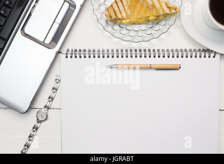 Business concept for woman with laptop, blank paper notepad, pen , ladies watch, cup of tea and toasted snack on white desk close up - overhead photo  Foto Stock