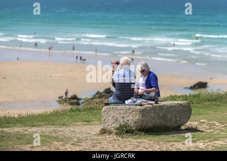 Anziani vacanzieri seduti su una roccia sul promontorio che si affaccia Fistral Beach in Newquay, Cornwall. Foto Stock