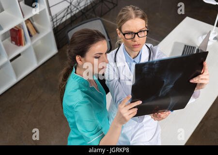 Medico grave in occhiali e infermiere esaminando immagine a raggi x in ospedale Foto Stock