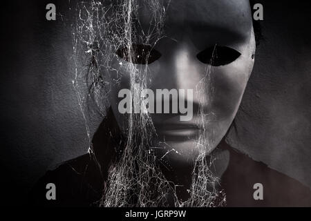 Misteriosa donna in nero che indossa maschera bianca nascosto dietro spider web,scary sfondo per la copertina del libro Foto Stock