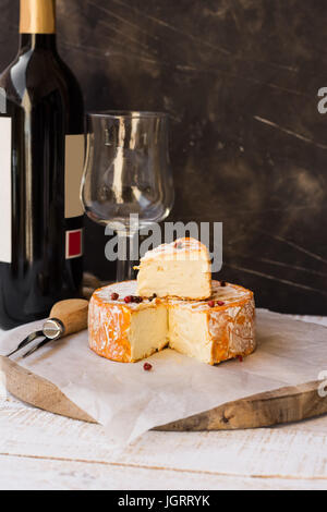 Il francese munster formaggio con scorza di arancia, pepe rosso calli, fetta tagliata, forcella,bottiglie di vino e vetro, stile rustico Foto Stock