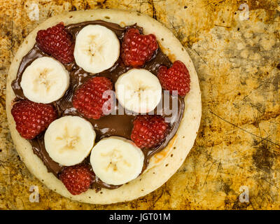 Pancake con cioccolato da spalmare con banana e lamponi seduto su una teglia da forno Foto Stock