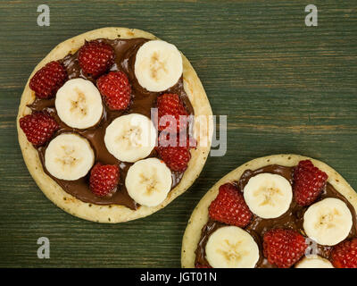 Pancake con cioccolato da spalmare con banana e lamponi contro uno sfondo verde Foto Stock