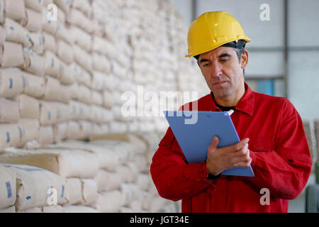 Lavoratore nel magazzino di distribuzione accanto al grande pila di sacchi a grande magazzino nel moderno stabilimento. Foto Stock