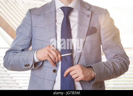 Imprenditore irriconoscibile impostazione del tirante rettilineo regolando il suo tie pin. Retroilluminazione con una lente effetto flare. Foto Stock