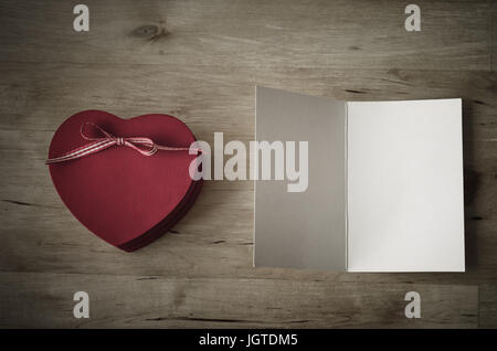 Scatto dall'alto di un dipinto di rosso in legno a forma di cuore confezione regalo con nastro prua e una volta aperta la scheda Messaggi di saluto, lasciata vuota per un messaggio.effetto vintage con Foto Stock