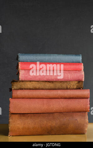 Chiudere il colpo di una pila di vecchi, trasandato, ben utilizzati libri di testo impilati in una pila su una scrivania di fronte a una lavagna. Copia spazio sopra. Foto Stock