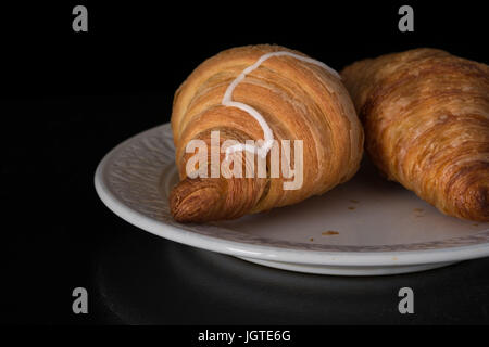 La cannella semiperni croissant sulla piastra bianca su sfondo nero Foto Stock