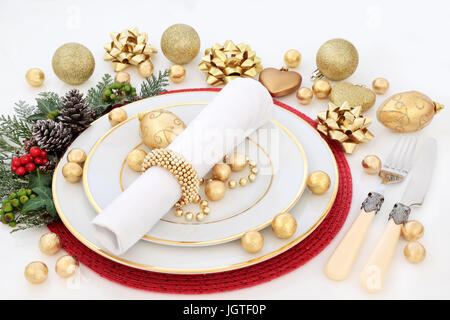 Cena di Natale messa in tavola con piatti di porcellana, igienico, oro ninnolo decorazioni, posate, agrifoglio, vischio, ivy e abeti bianchi su sfondo bianco Foto Stock