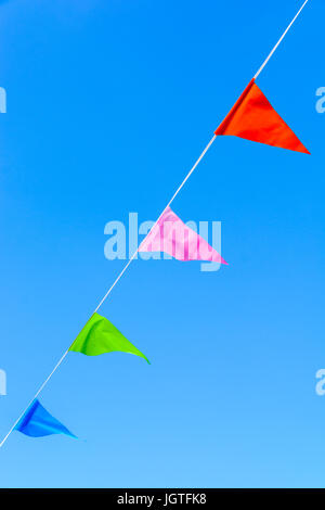 Bunting con colorate bandiere triangolari che soffiano nel vento contro il cielo blu. Foto Stock