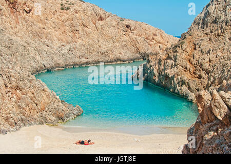 Giovane donna caucasica in costume nero giacente sulla selvaggia spiaggia appartata guardando il turchese laguna blu sulla calda giornata di sole in Seitan Limania, Chania, Cre Foto Stock