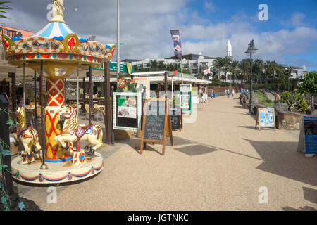 I bambini di merry-go-round e negozi presso il lungomare di Playa Dorada Beach, Playa Blanca, Lanzarote, Isole canarie, Spagna, Europa Foto Stock
