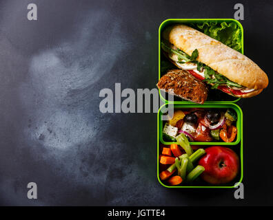 Estrarre il cibo scatola di pranzo con tonno e uova Sandwich, insalata greca e verdure su lavagna sfondo spazio di copia Foto Stock