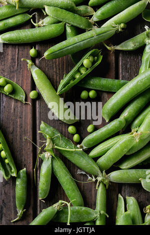 Giovani organico pisello verde baccelli di piselli e sopra il vecchio scuro listoni in legno sfondo. Vista da sopra con lo spazio. Raccolto, mangiare sano. Foto Stock
