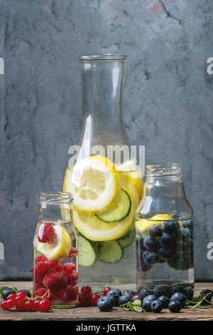Cetriolo di agrumi bacche Mirtilli e rasberry sassy sassi acqua per detox in bottiglie di vetro di legno su sfondo blu. Pulire mangiare, uno stile di vita sano Foto Stock