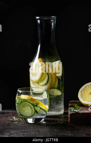 Citrus cetriolo sassy sassi acqua per detox in bottiglia di vetro scuro su sfondo nero. Pulire mangiare, uno stile di vita sano concetto, la luce del sole Foto Stock