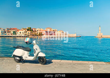 Cross-immagine elaborata di bianco in stile retrò scooter parcheggiato nel porto di Chania sulla soleggiata giornata estiva con la città vecchia e la luce veneziana house backgroun Foto Stock