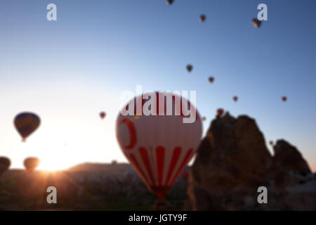 Vista offuscata su i palloni ad aria calda con simbolico turco sul blu chiaro alla luce del sole e cielo Camini di Fata formazioni rocciose di sunrise. Usare come sfondo Foto Stock