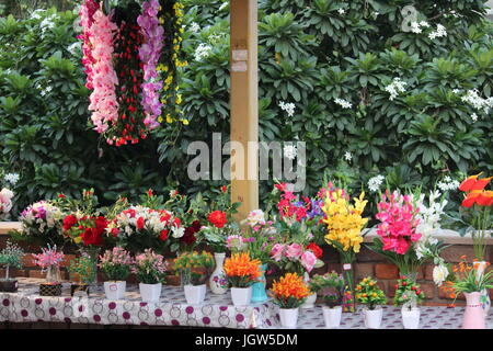 Fiori artificiali in vendita presso Dilli Haat, Pitampura, Delhi, India. Dietro di loro è un albero reale con fiori di colore bianco Foto Stock