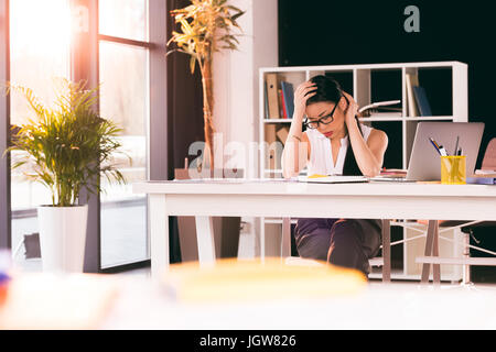 Stanco asian imprenditrice seduti al posto di lavoro e il lavoro in ufficio moderno Foto Stock