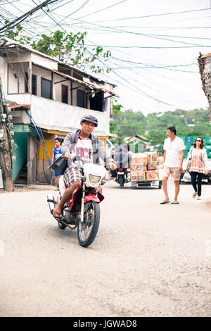 Uomo in sella a una motocicletta con la gente che camminava per le strade di Boracay. Foto Stock