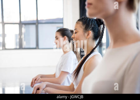 Vista laterale di giovani donne in sportswear meditando a lezione di yoga Foto Stock